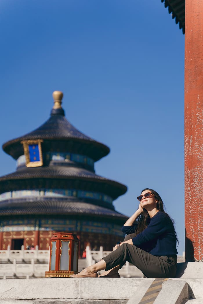 Una turista sentada frente al Templo del Cielo en Pekín, China, bajo un cielo azul despejado.
