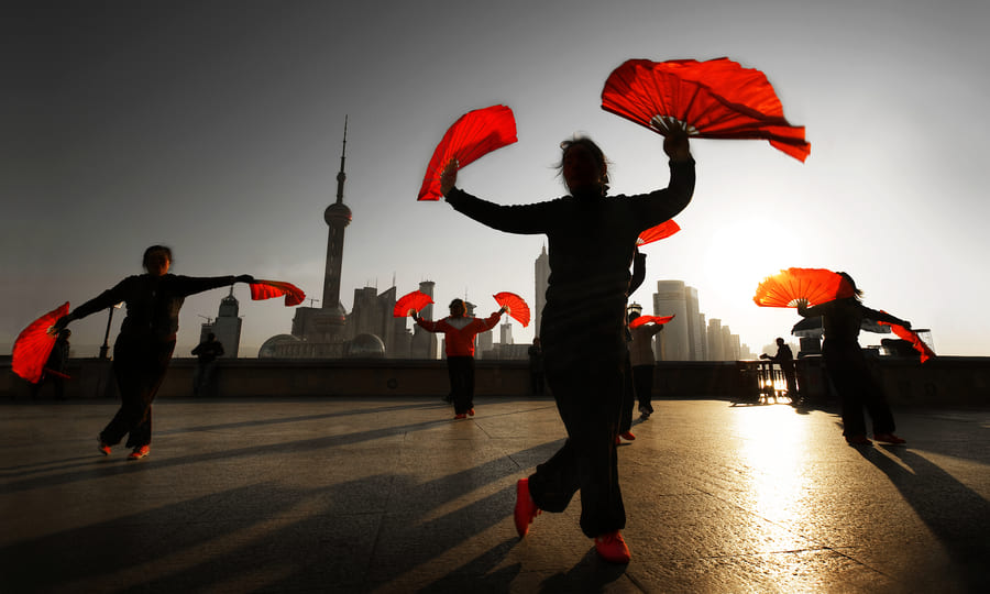 Bailarines interpretando una danza tradicional china con abanicos al amanecer en el Bund, con el horizonte de Shanghái de fondo.