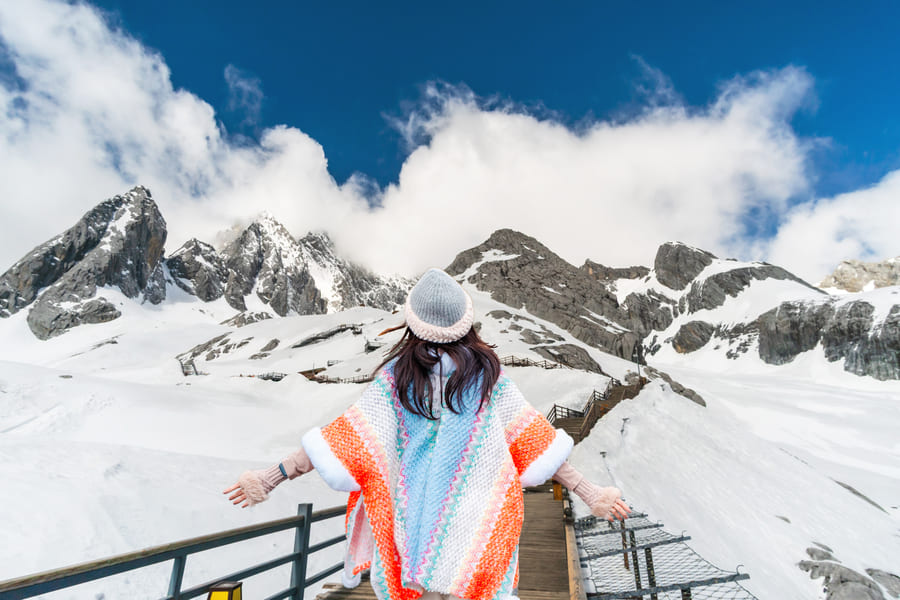 Una viajera con un colorido poncho contempla los picos nevados de la Montaña Nevada del Dragón de Jade en Lijiang.