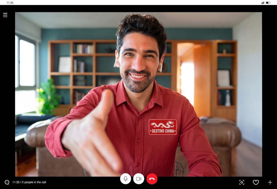 Un hombre sonriente con una camiseta de Destino China ofrece un apretón de manos durante una videollamada de una reunión de negocios virtual.